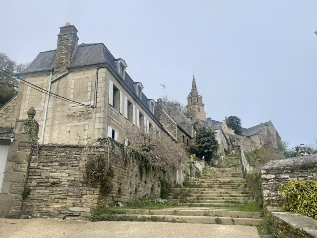 A staircase leading up to Brélévenez Church in Lannion, with the church spire peeking from the top. 라니옹 브렐레베네즈 성당으로 이어지는 계단, 언덕 위로 교회 첨탑이 살짝 보이는 모습.