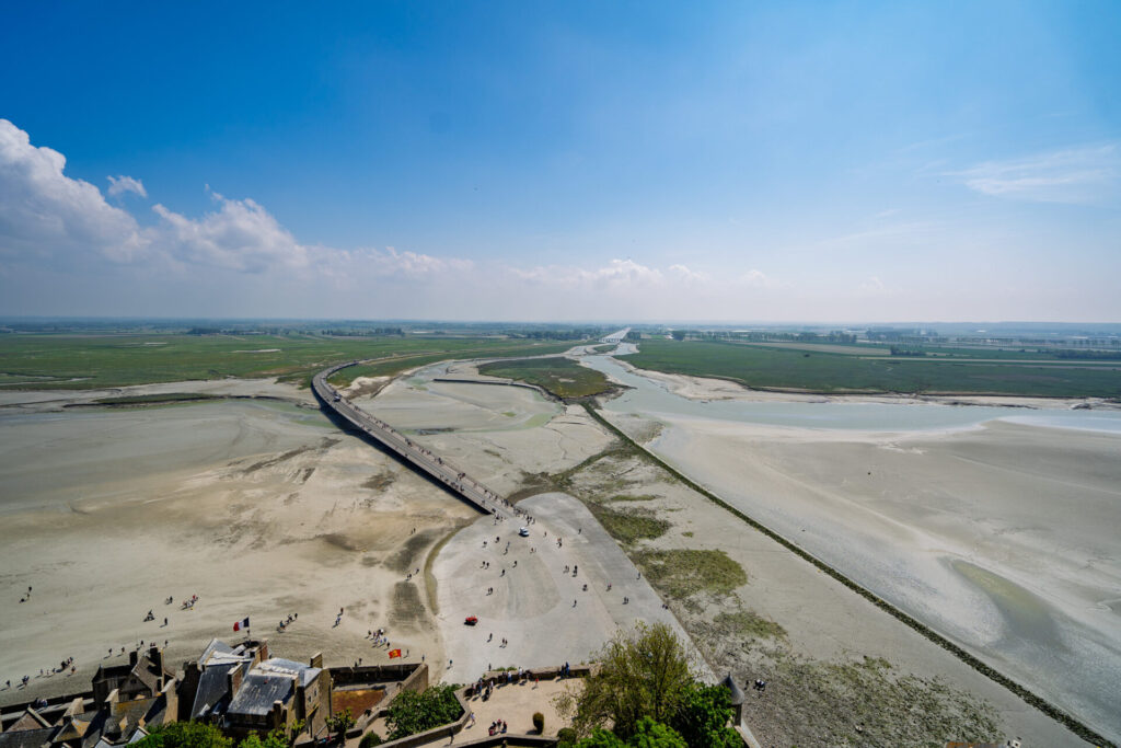 View from Mont Saint-Michel Abbey showing the mudflats, the Passerelle bridge, and tiny people visible on both 몽셍미셸 수도원에서 내려다본 뻘, 파세렐 다리, 그리고 그 위의 작은 사람들