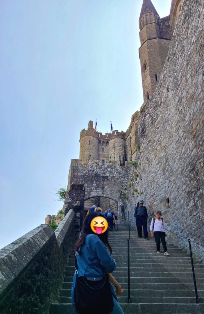 The final stone staircase leading up to Mont Saint-Michel Abbey, surrounded by towering medieval walls. 몽생미셸 수도원으로 올라가는 마지막 돌계단, 웅장한 중세 성벽이 감싸고 있는 모습.