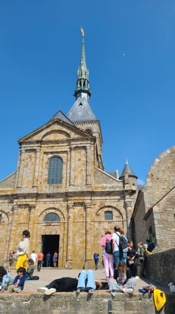 People lying on the West Terrace of Mont Saint-Michel Abbey, enjoying the warm sunlight and relaxing under the blue sky. 몽생미셸 수도원 서쪽 테라스에 누워 따뜻한 햇살을 즐기며 쉬고 있는 사람들.