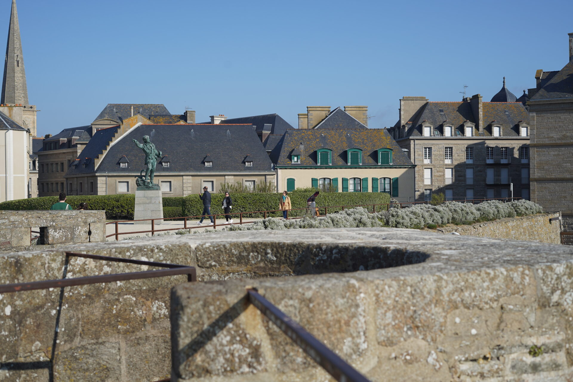 A view from the Saint-Malo city wall looking inward, featuring a bronze statue and the city's iconic stone buildings. 생말로 성벽 위에서 안쪽을 바라본 풍경으로, 청동 조각상과 특징적인 돌 건물들이 보이는 모습.