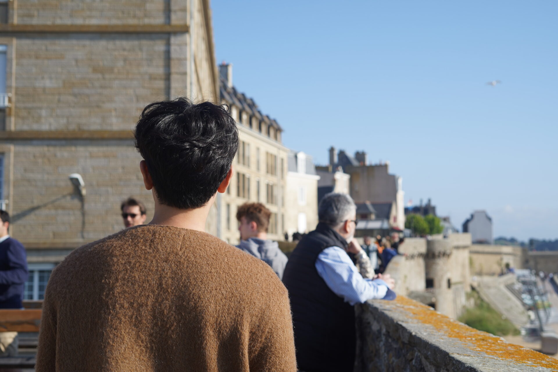 A person walking along the Saint-Malo city wall, with others enjoying the scenic promenade. 생말로 성벽 위를 걷고 있는 사람과 산책을 즐기는 사람들의 모습.