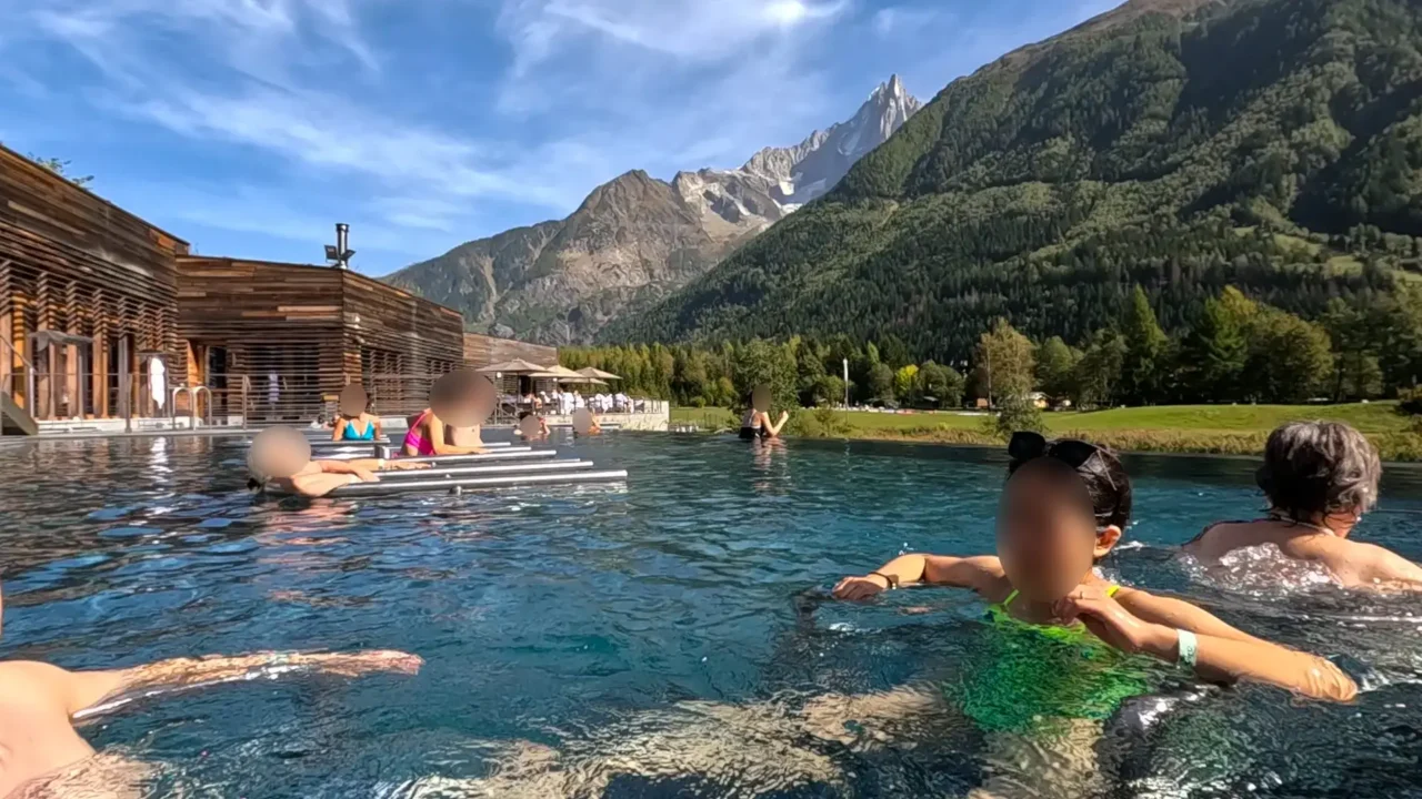 Relaxing in the infinity pool at QC Terme Chamonix, looking towards the left side with a view of wooden architecture and the surrounding mountains. QC Terme Chamonix 인피니티풀에서 왼쪽 방향을 바라본 모습, 나무 건축물과 산맥이 어우러진 풍경
