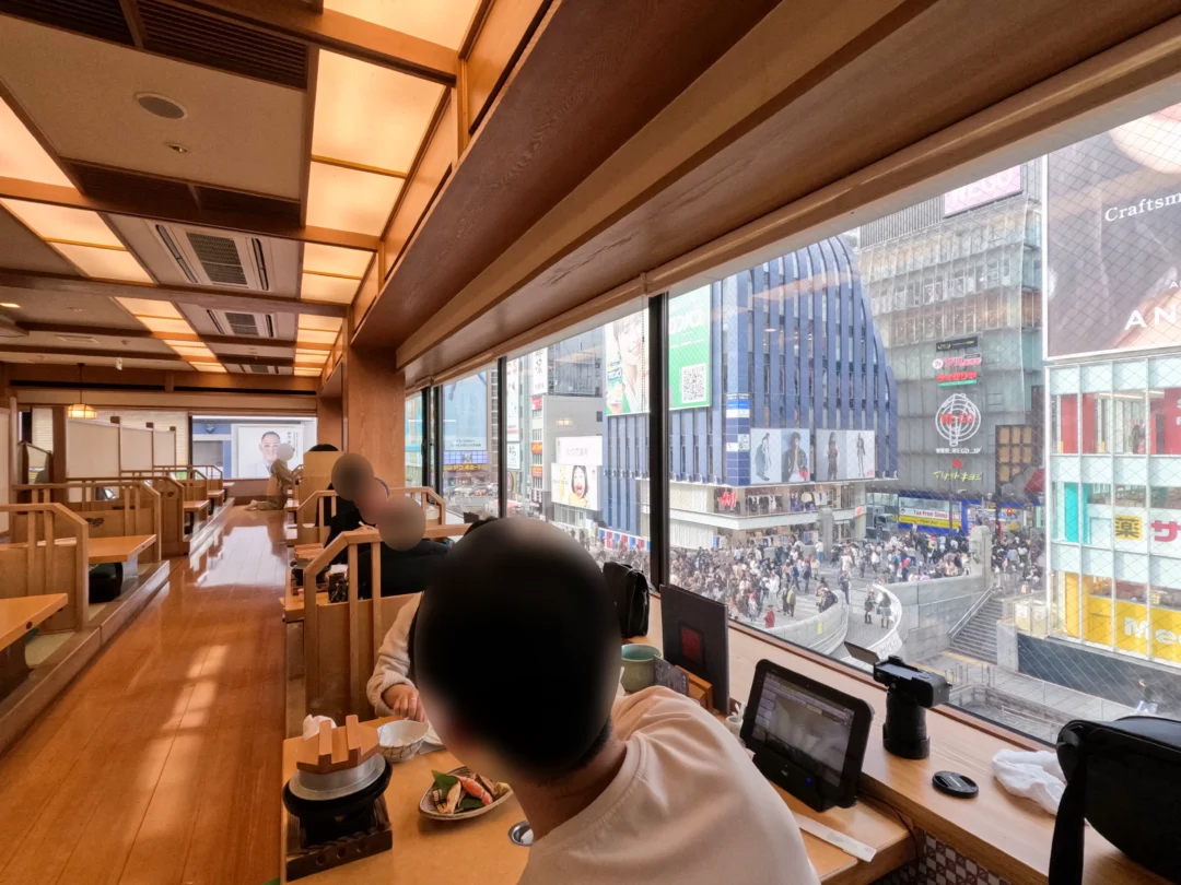 Inside view of Kani Doraku’s upper floor with traditional seating and a panoramic view of Dotonbori and Ebisu Bridge. 도톤보리와 에비스 다리를 내려다보는 카니도라쿠 상층부의 전통 좌석 공간