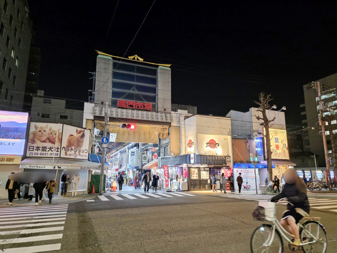 Main entrance to Kuromon Ichiba Market in Osaka at night, bustling with people and lights. 사람들과 불빛으로 북적이는 오사카 구로몬 시장 입구의 밤 풍경