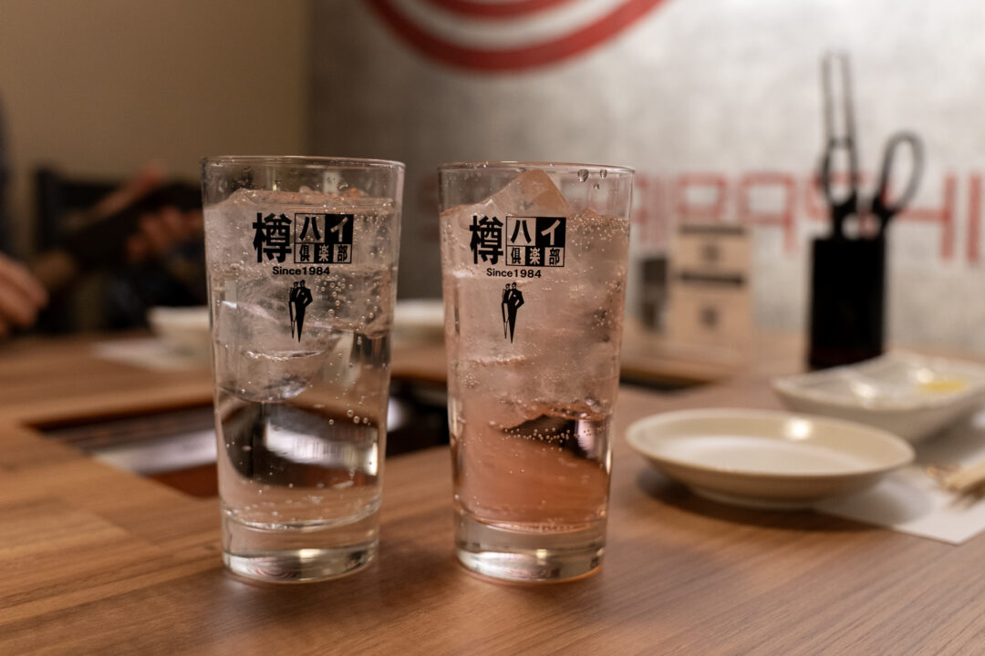 Two highball glasses filled with ice and drinks at Yakiniku Inyen - clear soda and pink grapefruit chuhai. 신사이바시야키니쿠 인연에서 제공되는 얼음 가득한 두 음료 - 투명한 사이다와 핑크빛 자몽 츄하이.