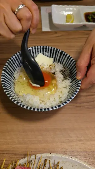 Mixing the TKG egg rice with soy sauce using a black spoon at Yakiniku Inyen. 신사이바시야키니쿠 인연에서 검은 숟가락으로 계란밥을 간장과 함께 비비는 모습.