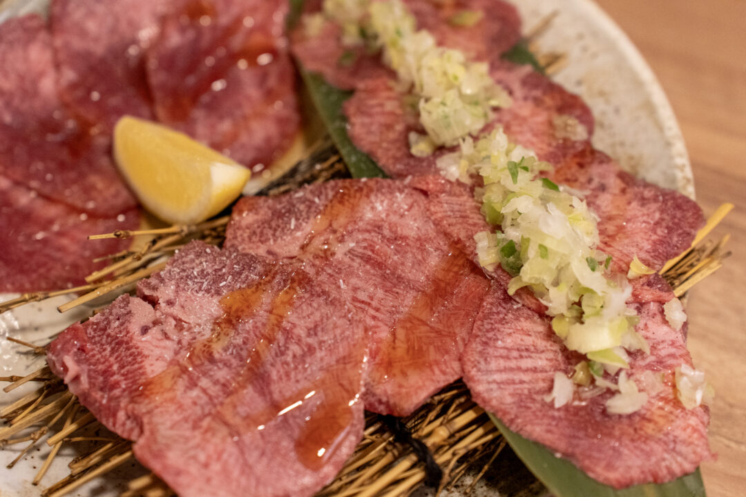 Close-up of thick-cut beef tongue slices with gloss from light marinade at Yakiniku Inyen. 신사이바시야키니쿠 인연의 두꺼운 우설 슬라이스 클로즈업, 가벼운 양념으로 인한 윤기가 있음.
