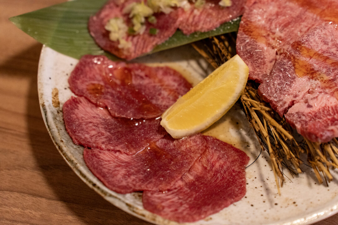 Close-up of thinly sliced beef tongue with lemon wedge at Yakiniku Inyen. 신사이바시야키니쿠 인연의 얇게 썬 우설과 레몬 조각 클로즈업.